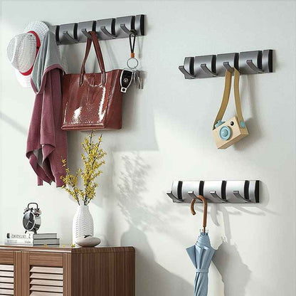 Porte-manteau mural moderne en aluminium avec crochets relevables, portant un chapeau, un sac en cuir et des clés, installé à côté d'un meuble de rangement en bois.