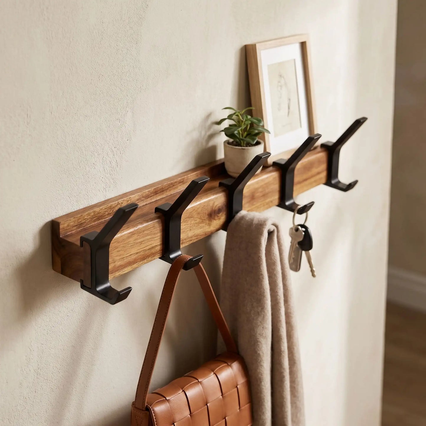 Détail d'un porte-manteau en bois d'hévéa massif avec étagère décorative et crochets en aluminium noir dans une entrée lumineuse.