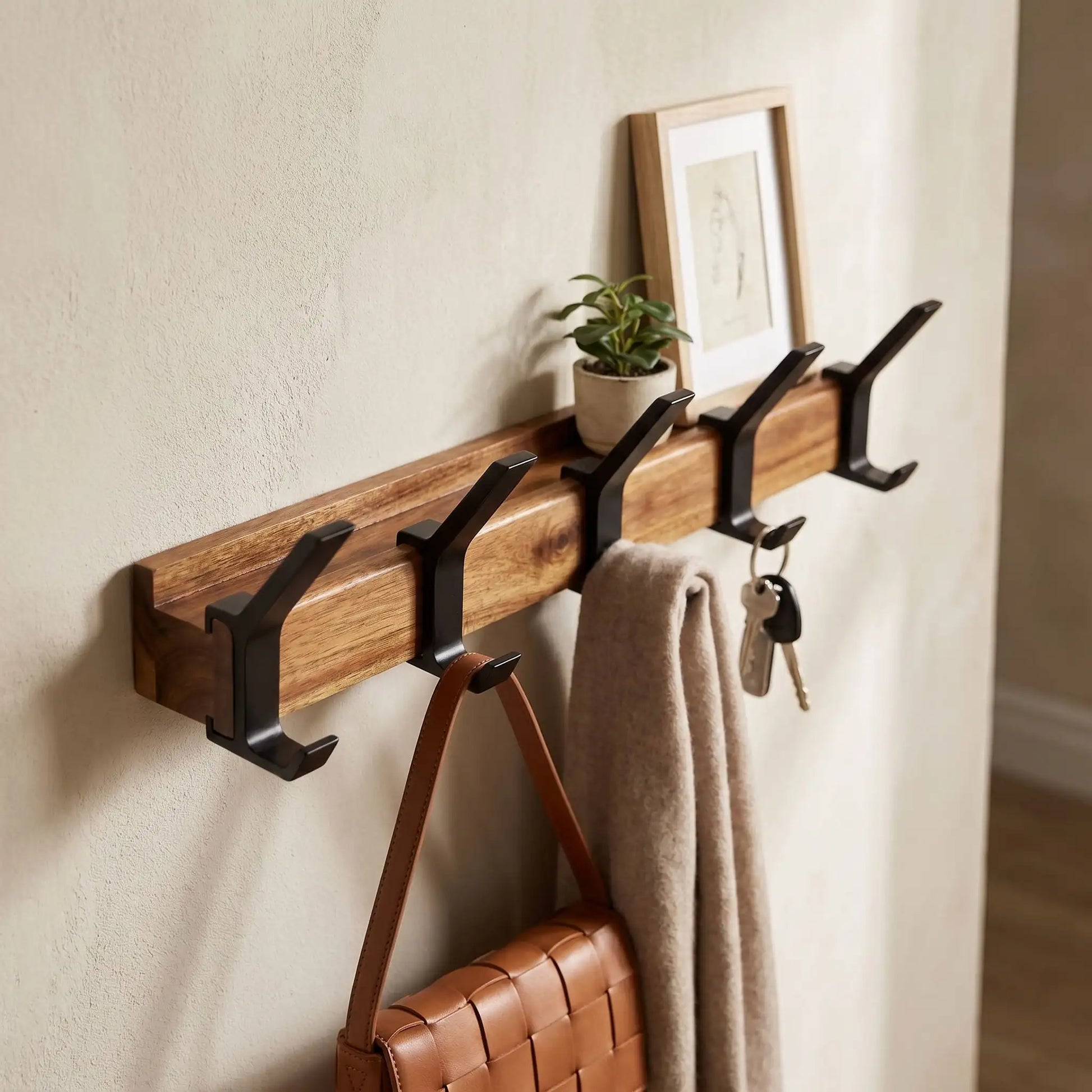 Détail d'un porte-manteau en bois d'hévéa massif avec étagère décorative et crochets en aluminium noir dans une entrée lumineuse.