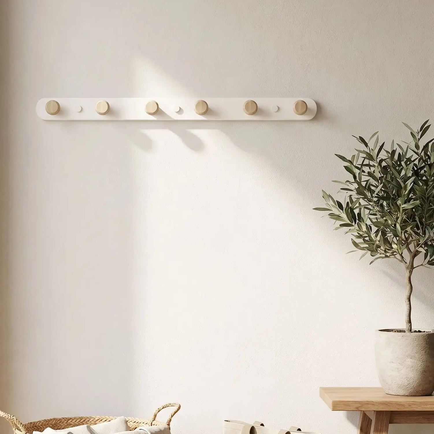 Porte-manteau mural 6 crochets en bois et blanc installé dans une entrée lumineuse à côté d'une plante verte.