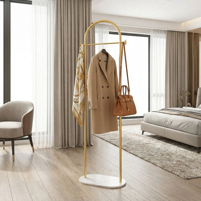 Porte-manteau design Soma en finition Or brossé, présenté dans une chambre luxueuse avec des vêtements élégants pour souligner la qualité haut de gamme.