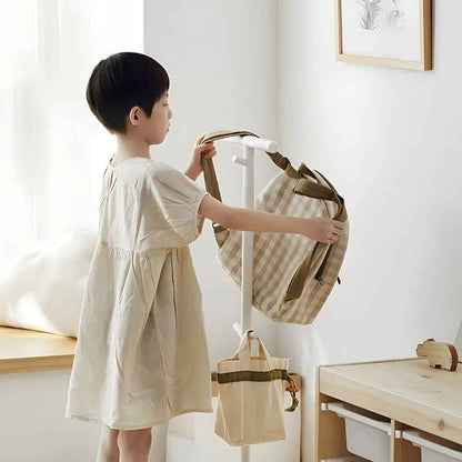 Enfant utilisant le porte-manteau enfant blanc à hauteur Montessori pour accrocher son sac de manière autonome.