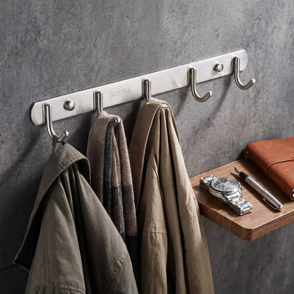Détail du porte-manteau mural Le Pêcheur en acier inoxydable brossé argenté à côté d'accessoires élégants, illustrant la finition haut de gamme et la durabilité du matériau.
