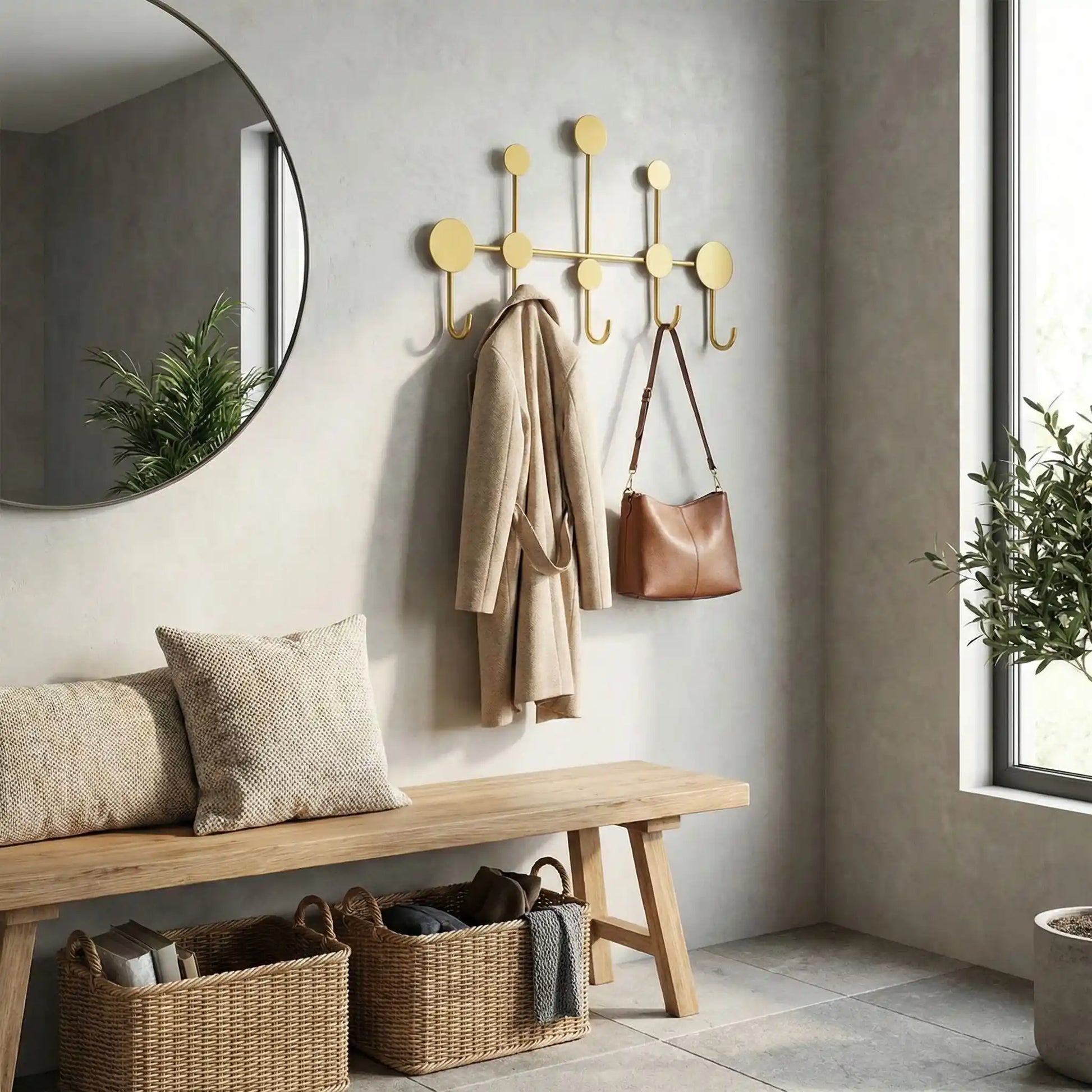 Mise en situation d'un porte-manteau mural design Orno en fer forgé doré dans une entrée moderne avec miroir rond, banc en bois et paniers de rangement.