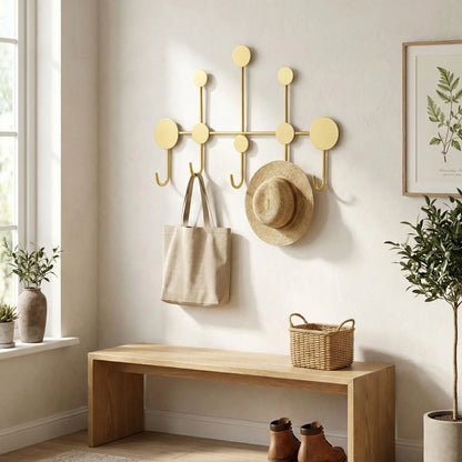 Porte-manteau mural design en fer forgé doré Orno installé dans une entrée lumineuse au-dessus d'un banc en bois.