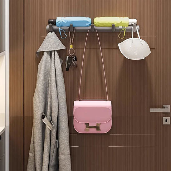 Porte-manteau mural Alumure en aluminium gris sidéral supportant un long manteau, un sac à main rose et deux parapluies.