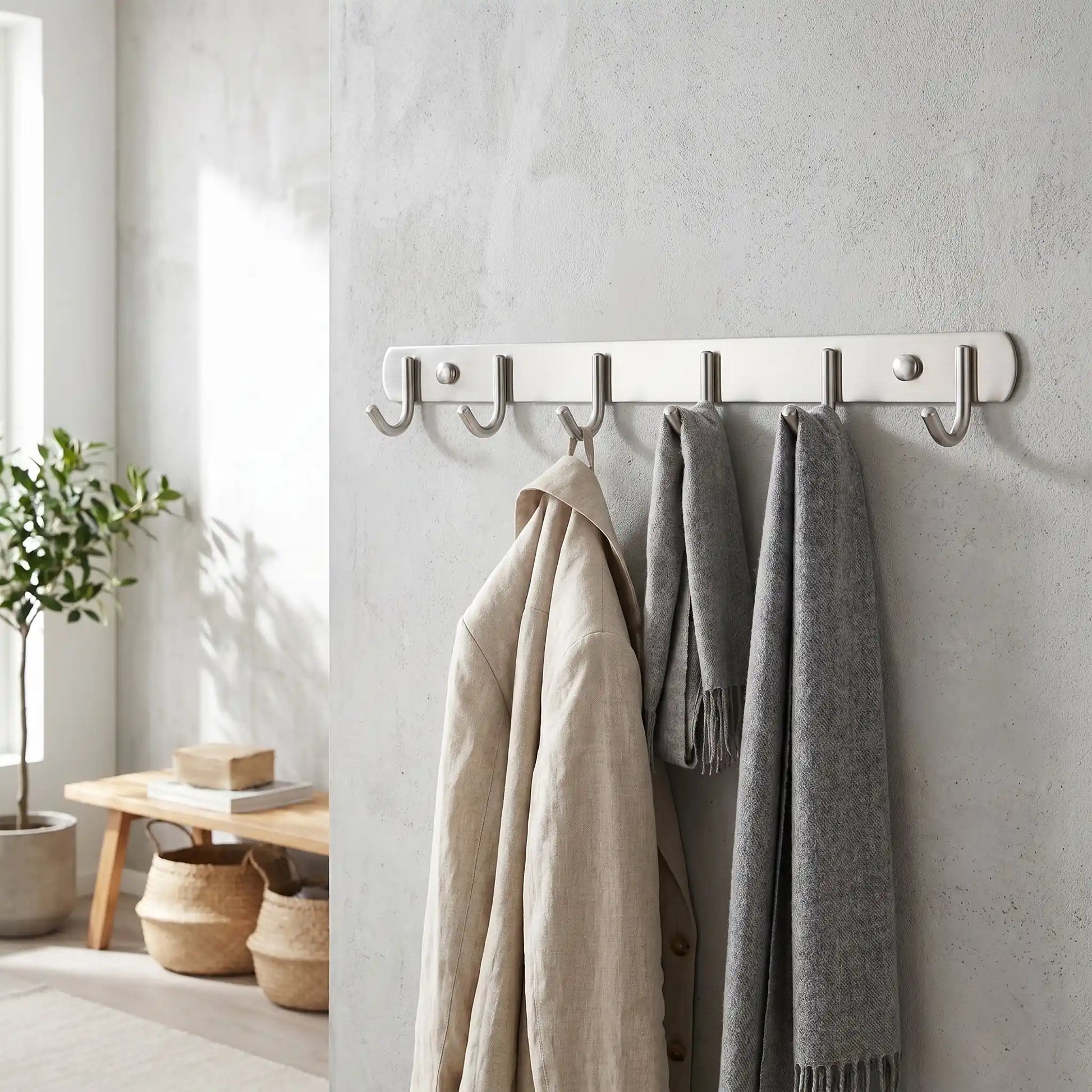 Porte-manteau mural Le Pêcheur en acier inoxydable avec 6 crochets simples, supportant des manteaux et écharpes dans une entrée lumineuse et moderne.