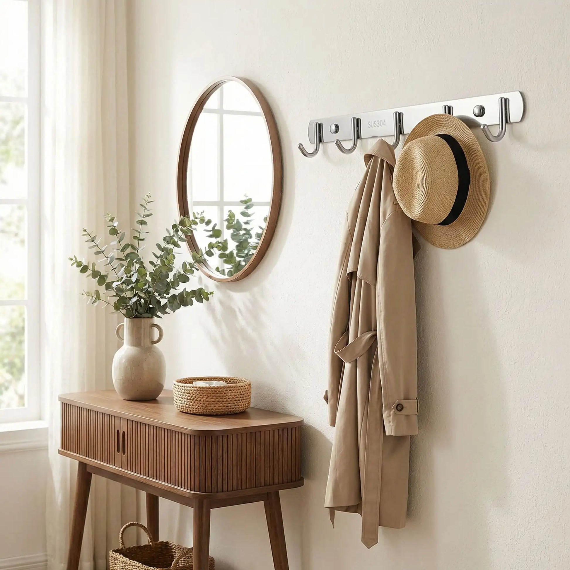 Porte-manteau mural Le Pêcheur en inox brossé installé dans une entrée élégante avec miroir rond, console en bois et plante verte.