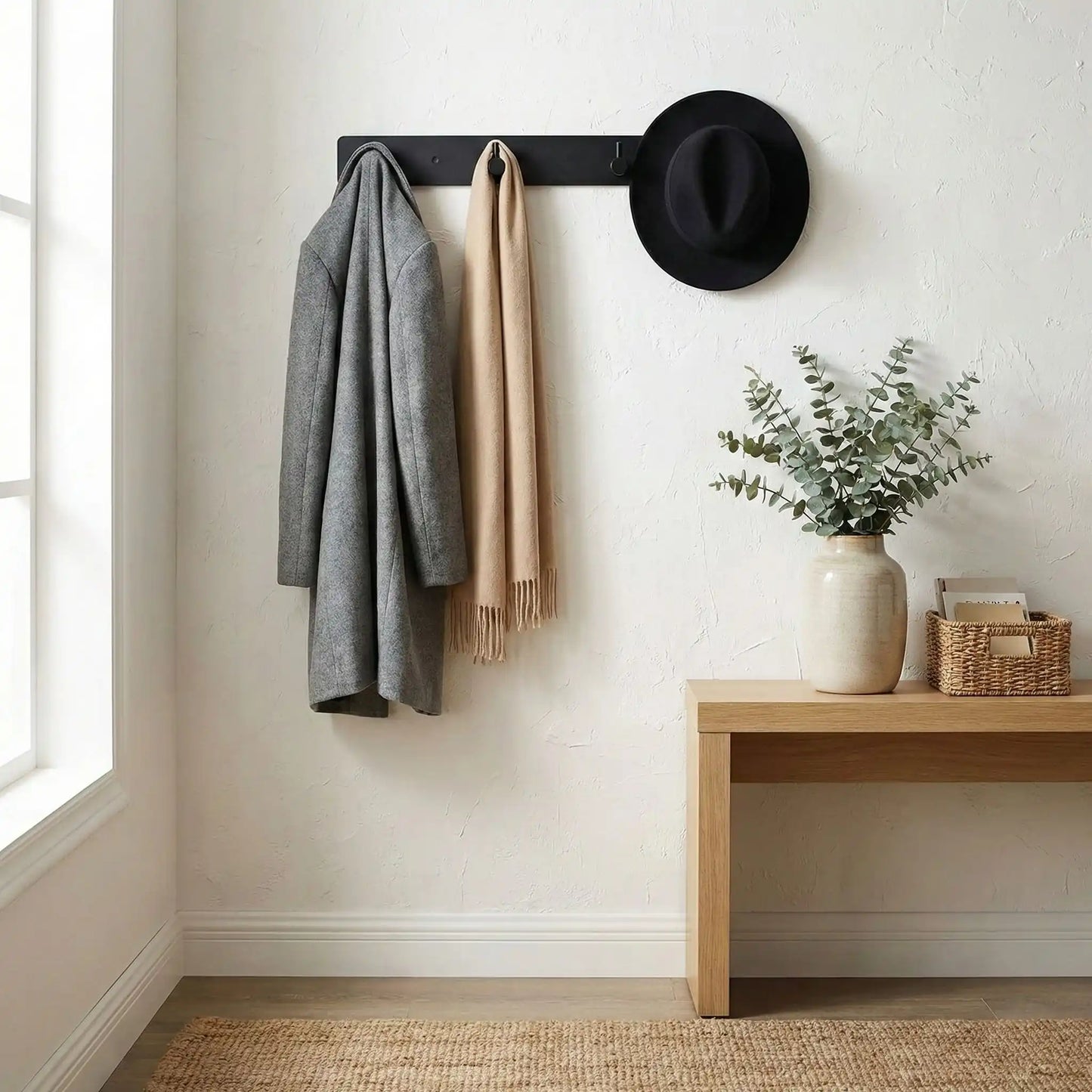 Porte-manteau mural noir mat supportant une veste et un chapeau, illustrant sa grande capacité de charge.