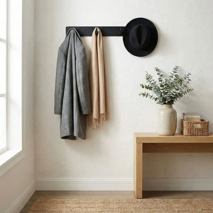 Porte-manteau mural noir mat supportant une veste et un chapeau, illustrant sa grande capacité de charge.