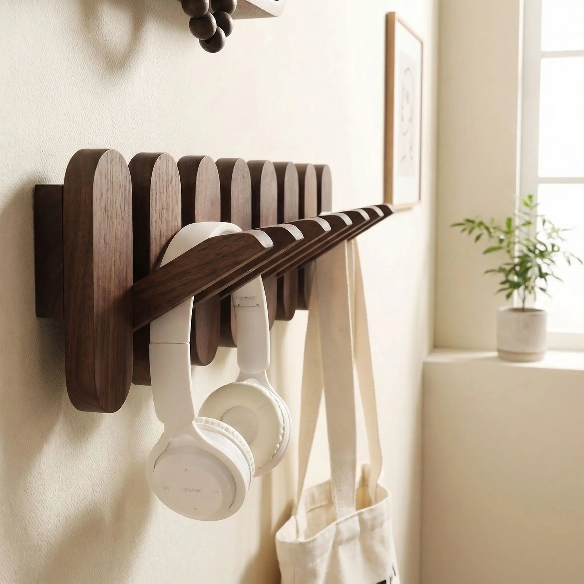 Porte-manteau mural design en noyer massif avec crochet rabattable ouvert tenant un casque audio blanc.