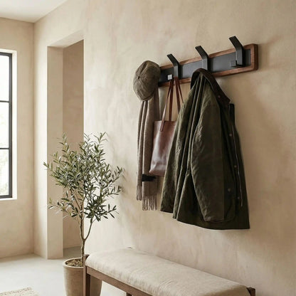 Porte-manteau patère mural en bois massif et métal noir avec manteaux et accessoires, installé au-dessus d'un banc dans une entrée lumineuse.