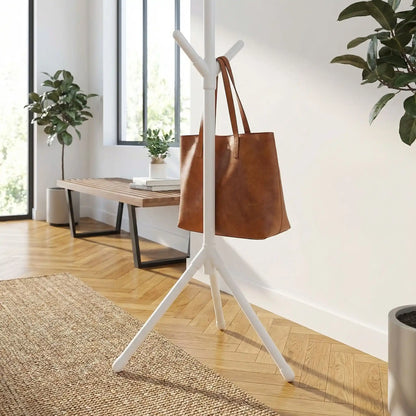 Porte-manteau sur pied blanc laqué au design branche avec sac en cuir marron suspendu, style scandinave et moderne.