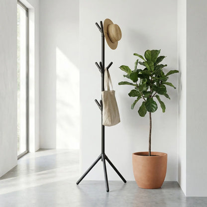 Porte-manteau sur pied noir mat au design organique avec chapeau et sac, installé à côté d'une plante verte dans une entrée moderne.