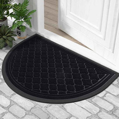 Tapis d'entrée demi-lune noir obsidienne avec bordure antidérapante posé sur un sol en pavés devant une porte blanche.